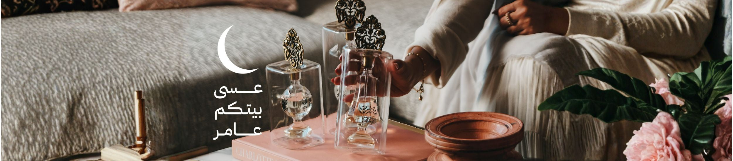 Three glass perfume bottles on a pink tray with a person's hand holding one bottle, sitting on a couch.